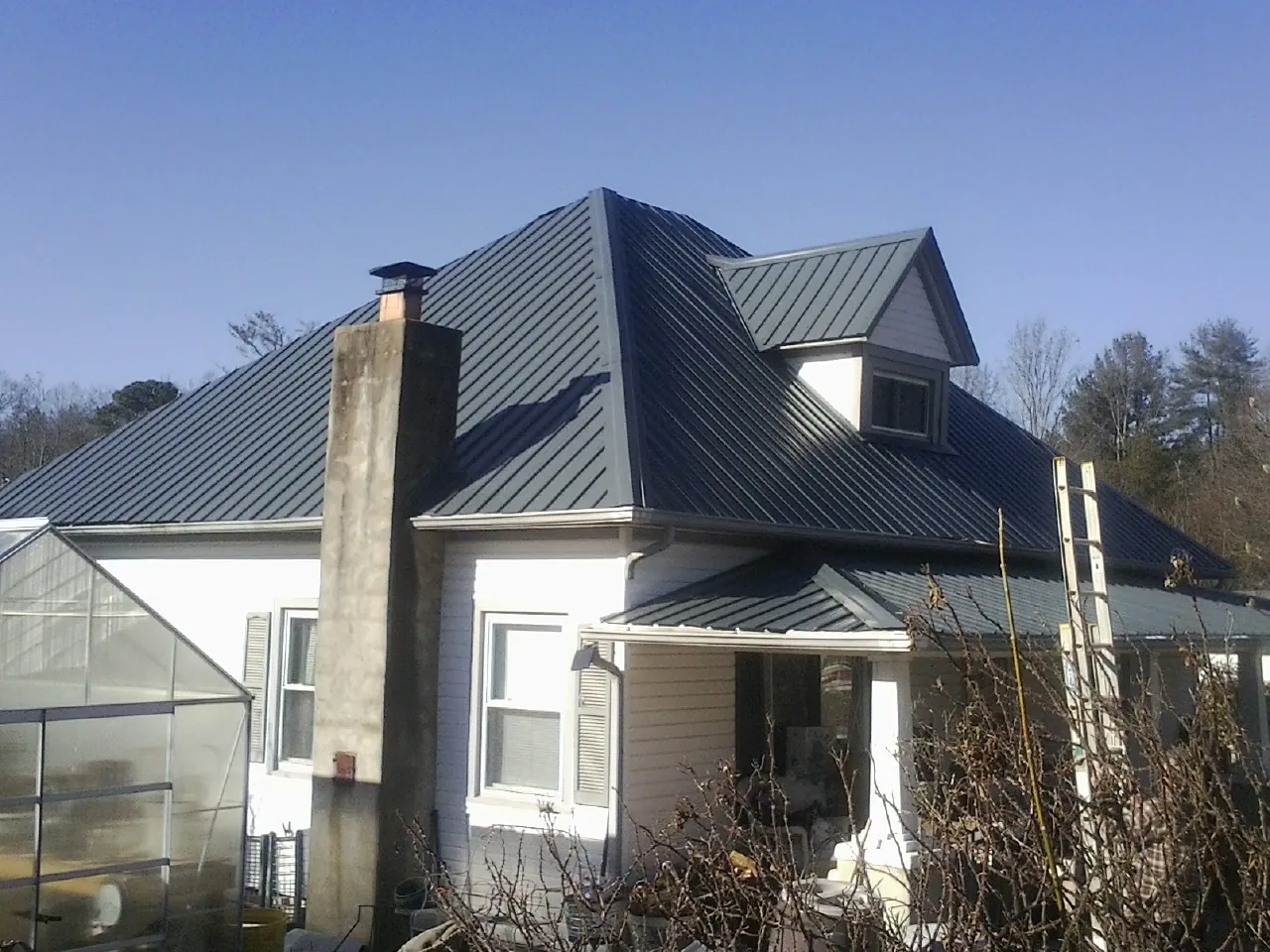 Dark blue standing seam metal roof on a white farmhouse with dormer — Slate & Tile Roof Repair by Roofing Brothers in Long Lake