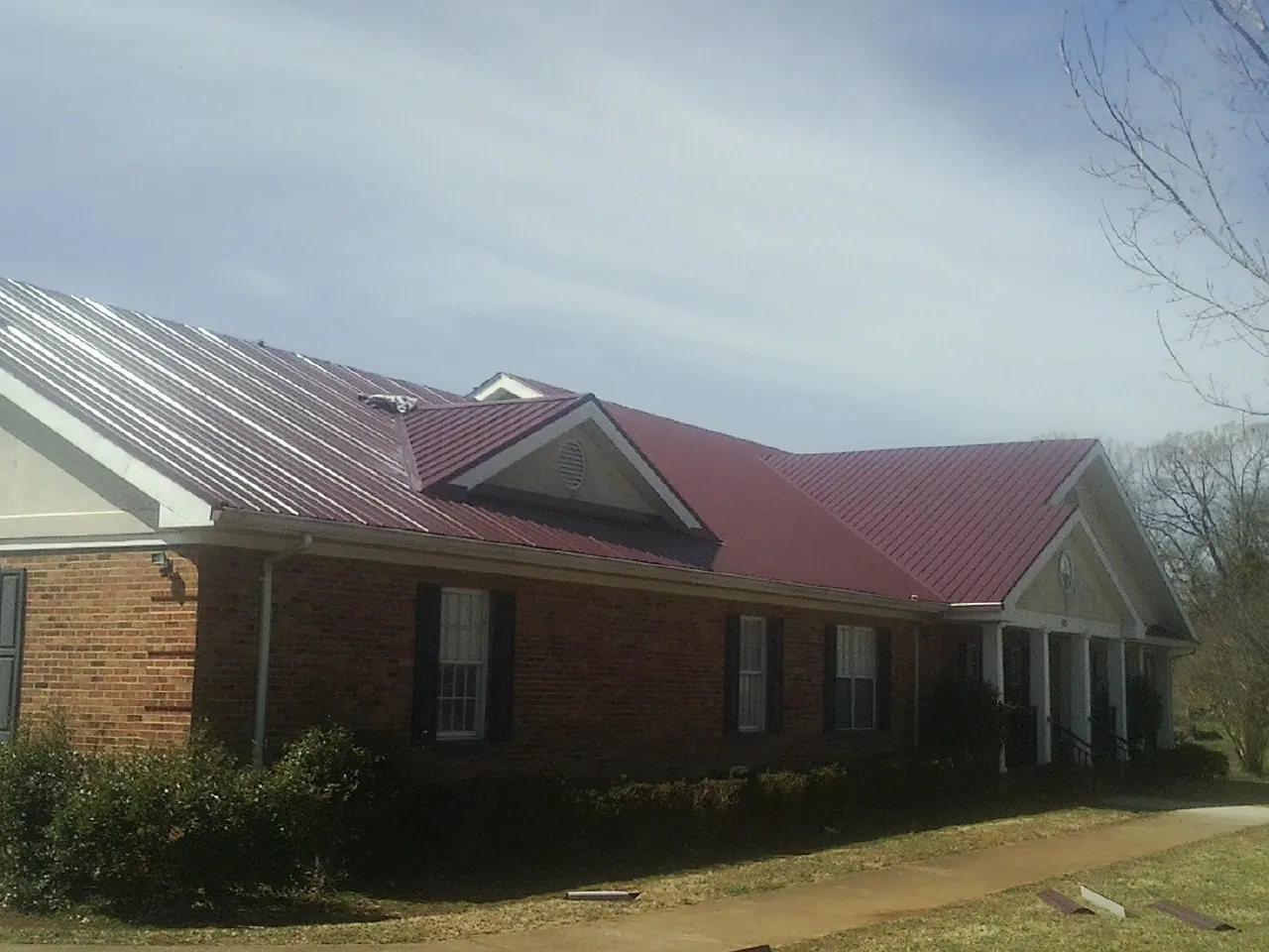 Red metal roof with gabled entries on a long brick building, from a Hail Damage Roof Repair job in Long Lake