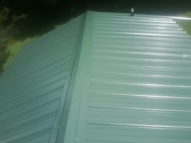 New green metal panels meeting at the ridge of a roof — Flat Roof Repair work by our crew in Long Lake