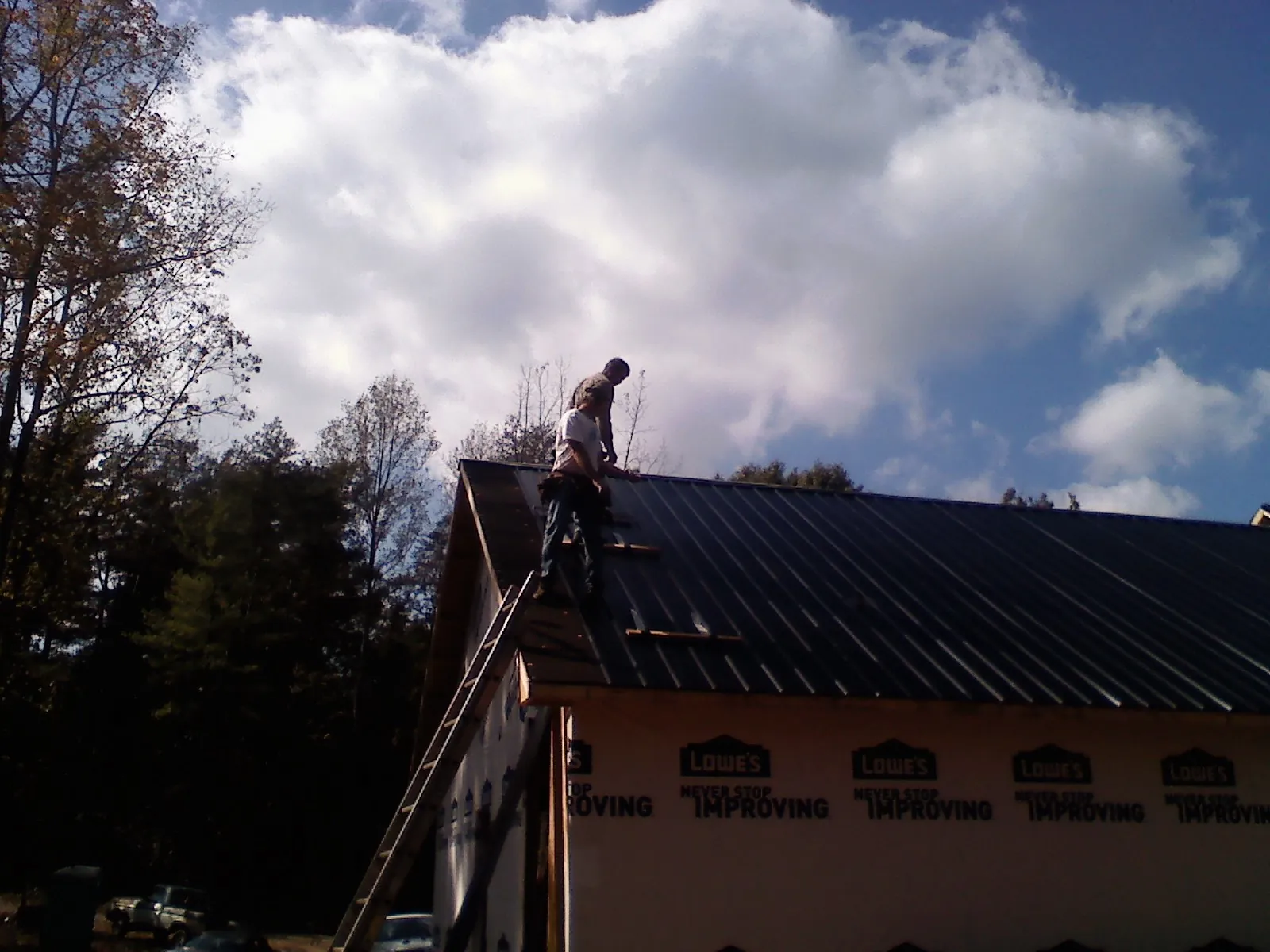 Roofer fastening dark metal panels high against a cloudy sky, from a Roof Inspection job in Long Lake