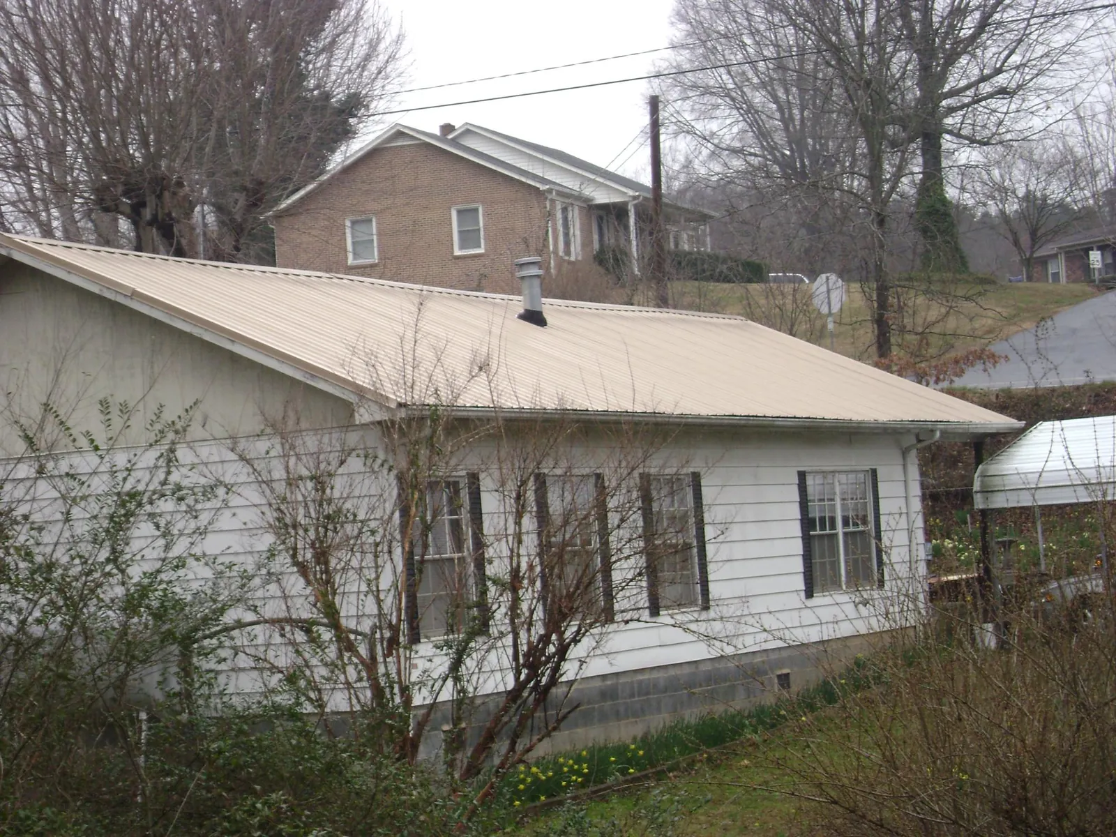 Tan metal roof on a white sided house set into a hillside — Commercial Roofing by Roofing Brothers in Long Lake