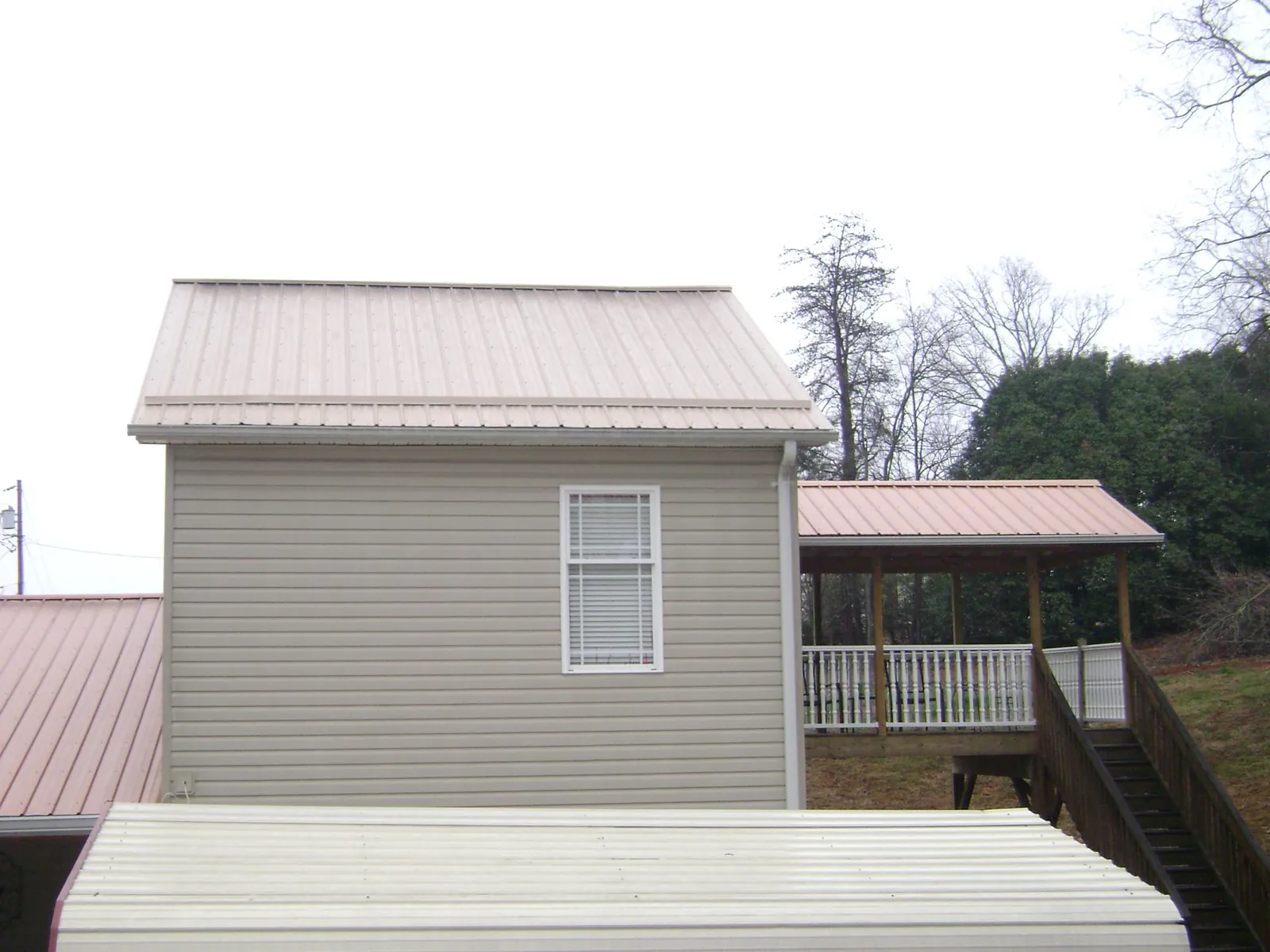 Tan metal roofs on a two story addition and attached porch, from a Roof Replacement job in Long Lake